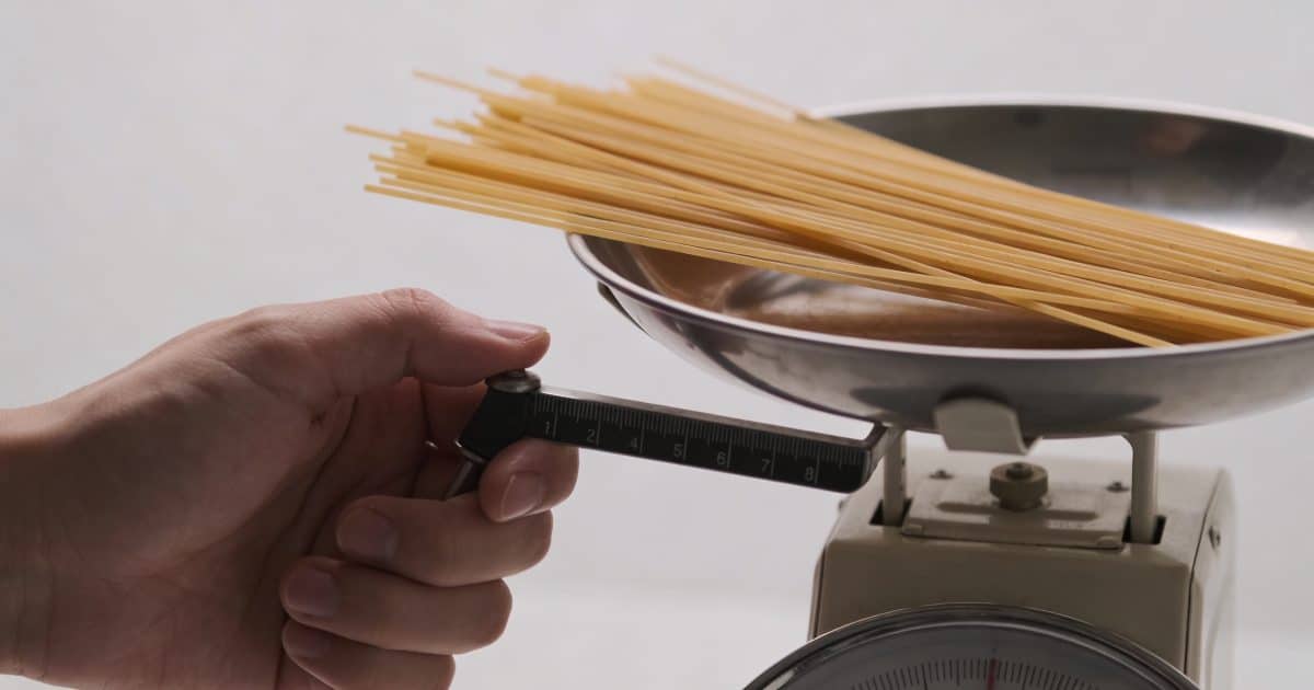 Main tenant une balance de cuisine pesant des spaghettis