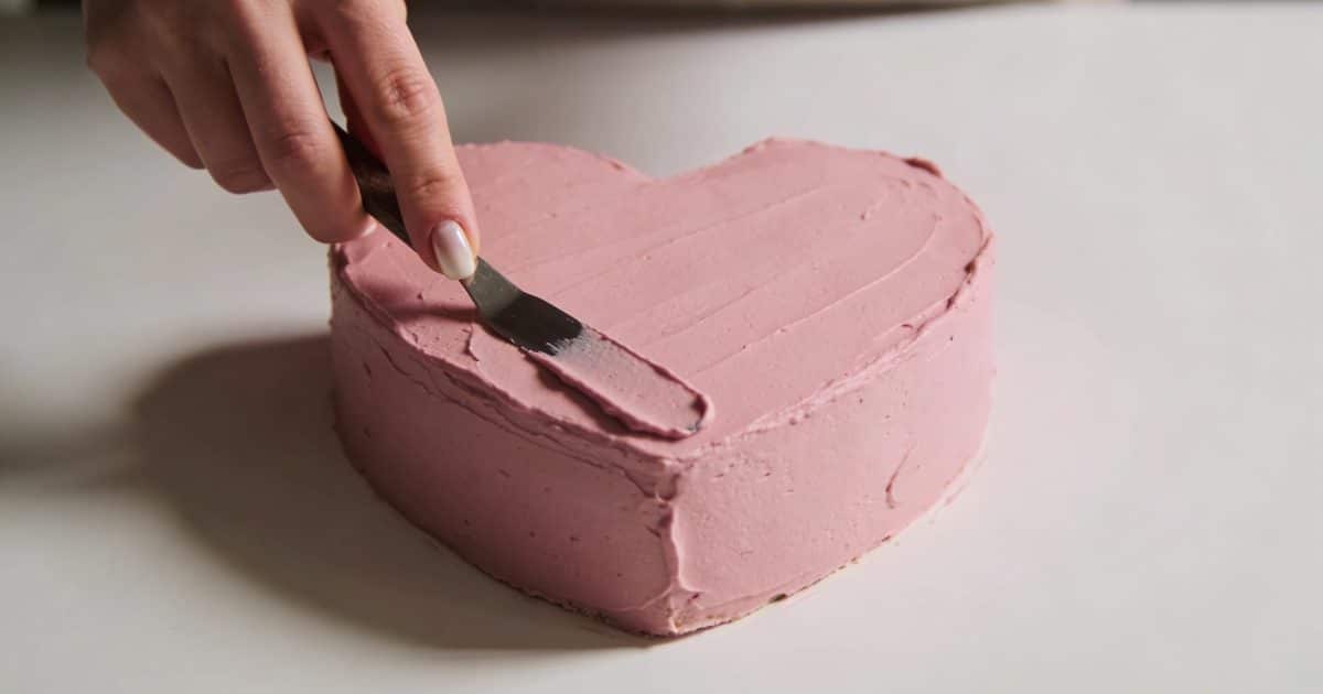 Main de femme decorant un gateau coeur rose