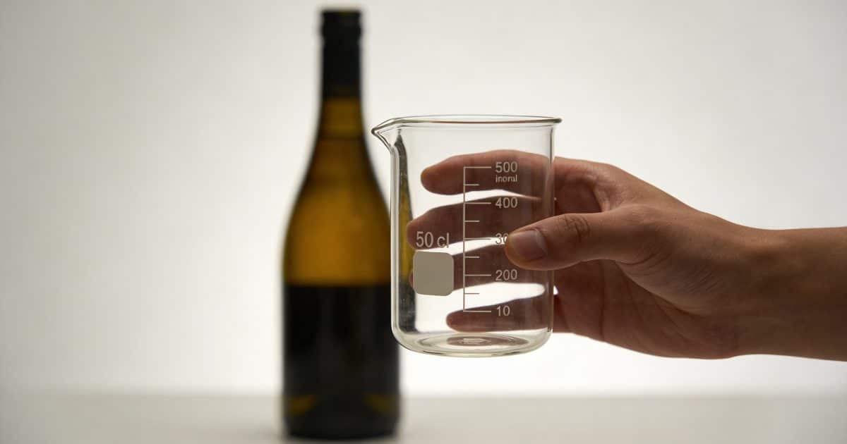 Main tenant un verre doseur 50 cl devant bouteille
