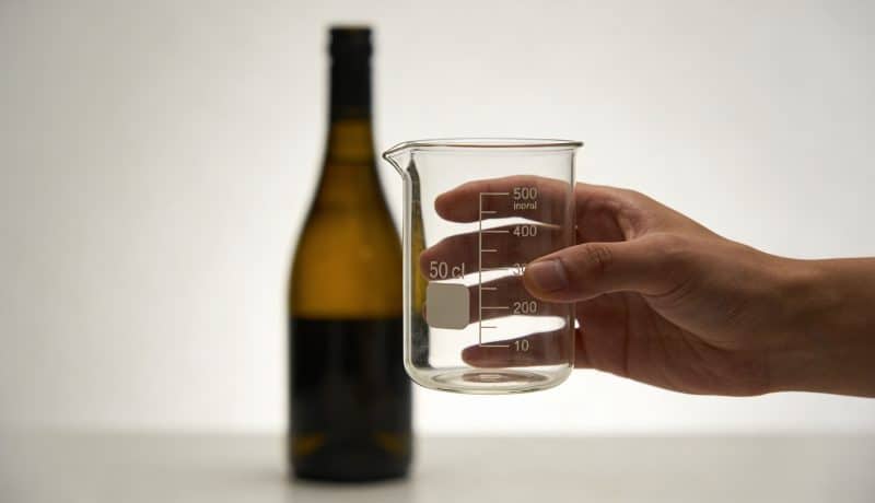 Main tenant un verre doseur 50 cl devant bouteille