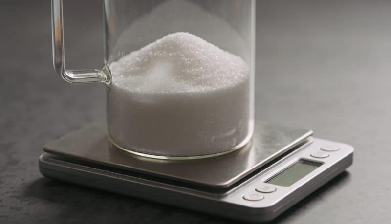 Verre doseur rempli de sucre blanc sur balance